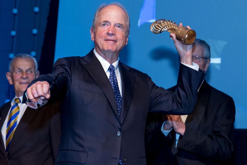 Peter Ueberroth holding an award as in pitching a ball.